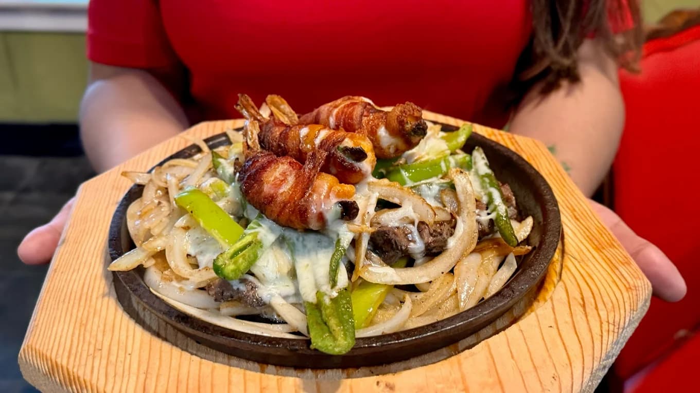 Sizzling fajitas with bacon-wrapped shrimp held by server at Las Piñatas Kitchen